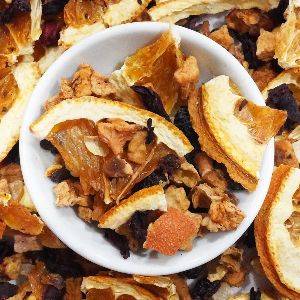 A close-up overhead shot of a white bowl filled with dried citrus slices, amber syrup pieces, and dark dried fruit pieces, surrounded by more of the same mixture.